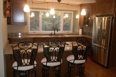 This is an example of a medium sized classic u-shaped kitchen in Cincinnati with a built-in sink, raised-panel cabinets, medium wood cabinets, laminate countertops, multi-coloured splashback, stainless steel appliances, medium hardwood flooring and an island.