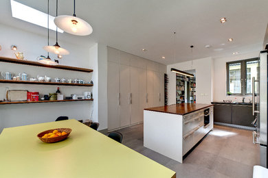Inspiration for a large contemporary galley kitchen/diner in London with flat-panel cabinets, stainless steel appliances, an integrated sink, white cabinets, wood worktops, cement flooring, a breakfast bar and grey floors.