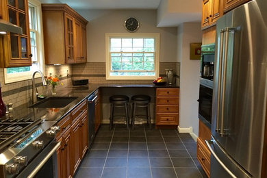 Example of a mid-sized classic u-shaped porcelain tile and gray floor kitchen design in Cleveland with an undermount sink, raised-panel cabinets, medium tone wood cabinets, granite countertops, beige backsplash, subway tile backsplash, stainless steel appliances and no island