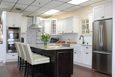 Example of a mid-sized transitional l-shaped dark wood floor kitchen design in Providence with a farmhouse sink, shaker cabinets, white cabinets, granite countertops, multicolored backsplash, mirror backsplash, stainless steel appliances and an island