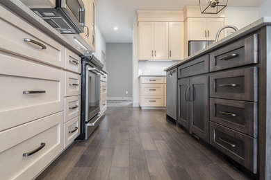 This is an example of a medium sized l-shaped open plan kitchen in Edmonton with a double-bowl sink, recessed-panel cabinets, beige cabinets, engineered stone countertops, white splashback, ceramic splashback, stainless steel appliances, medium hardwood flooring, an island and multi-coloured floors.