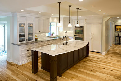 Large beach style l-shaped light wood floor eat-in kitchen photo in Miami with a farmhouse sink, raised-panel cabinets, white cabinets, marble countertops, white backsplash, subway tile backsplash and an island