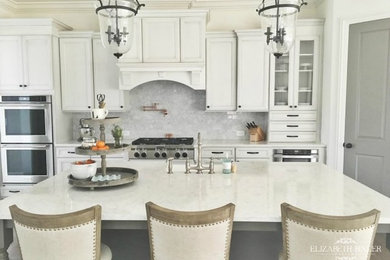 Example of a cottage medium tone wood floor eat-in kitchen design in Atlanta with a farmhouse sink, recessed-panel cabinets, white cabinets, quartz countertops, gray backsplash, stainless steel appliances and an island
