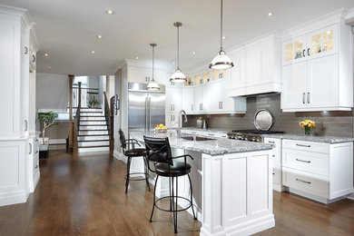 Example of a large farmhouse l-shaped medium tone wood floor and brown floor eat-in kitchen design in Toronto with white cabinets, granite countertops, glass tile backsplash, stainless steel appliances, an island, recessed-panel cabinets, a single-bowl sink, gray backsplash and gray countertops