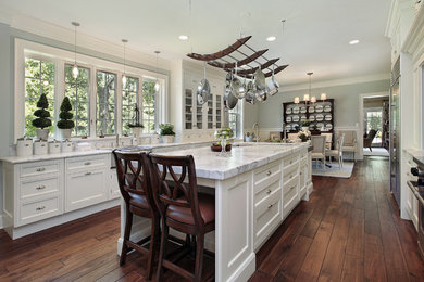 Inspiration for a large shabby-chic style galley medium tone wood floor open concept kitchen remodel in Los Angeles with a drop-in sink, raised-panel cabinets, white cabinets, stainless steel appliances, marble countertops, white backsplash, ceramic backsplash, an island and gray countertops