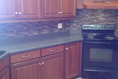 Immagine di una cucina a L di medie dimensioni con ante in legno bruno, paraspruzzi multicolore, elettrodomestici neri, pavimento con piastrelle in ceramica e nessuna isola