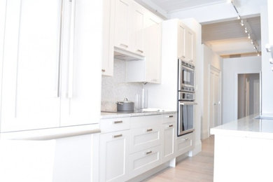 Example of a mid-sized trendy galley light wood floor enclosed kitchen design in Montreal with an undermount sink, raised-panel cabinets, white cabinets, granite countertops, metallic backsplash, cement tile backsplash, stainless steel appliances and beige countertops