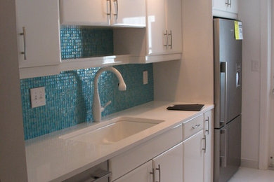マイアミにある中くらいなエクレクティックスタイルのおしゃれなキッチン (フラットパネル扉のキャビネット、白いキャビネット、青いキッチンパネル、ガラスタイルのキッチンパネル、シルバーの調理設備、セラミックタイルの床、アイランドなし) の写真
