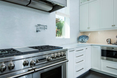 Bild på ett stort kök, med vita skåp, stänkskydd i sten, rostfria vitvaror och en köksö