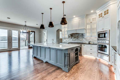 Example of a large transitional u-shaped medium tone wood floor and brown floor eat-in kitchen design in Cleveland with a drop-in sink, recessed-panel cabinets, white cabinets, granite countertops, gray backsplash, marble backsplash, stainless steel appliances and an island