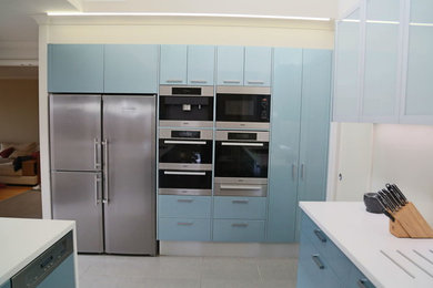 Diseño de cocina minimalista con armarios con paneles lisos, puertas de armario azules, electrodomésticos de acero inoxidable y suelo de baldosas de porcelana