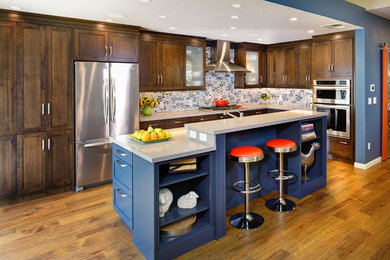 Trendy single-wall medium tone wood floor kitchen photo in Sacramento with recessed-panel cabinets, dark wood cabinets, solid surface countertops, multicolored backsplash, stainless steel appliances and an island