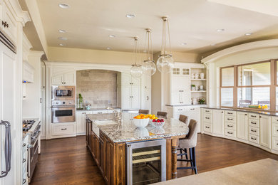 Example of a large transitional u-shaped medium tone wood floor eat-in kitchen design in Dallas with a farmhouse sink, shaker cabinets, white cabinets, granite countertops, beige backsplash, stone tile backsplash, stainless steel appliances and an island