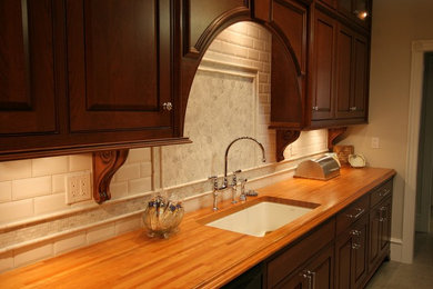Large arts and crafts galley travertine floor and beige floor enclosed kitchen photo in Other with an undermount sink, shaker cabinets, dark wood cabinets, wood countertops, white backsplash, marble backsplash, black appliances and no island
