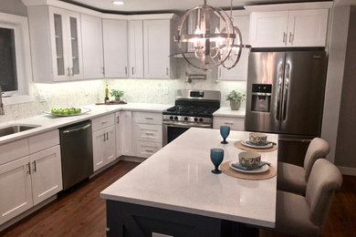 Example of a mid-sized transitional l-shaped medium tone wood floor and brown floor open concept kitchen design in New York with white cabinets, stainless steel appliances, an island, an undermount sink, shaker cabinets, quartz countertops and multicolored backsplash