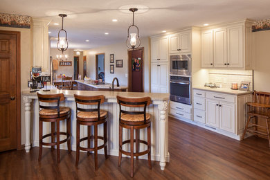 Eat-in kitchen - mid-sized traditional l-shaped medium tone wood floor eat-in kitchen idea in Other with an undermount sink, beaded inset cabinets, white cabinets, solid surface countertops, white backsplash, porcelain backsplash, stainless steel appliances and an island