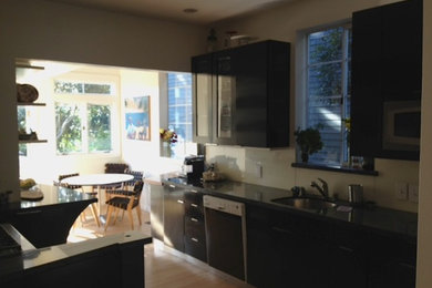 Example of a mid-sized minimalist u-shaped medium tone wood floor and brown floor eat-in kitchen design in San Francisco with an undermount sink, flat-panel cabinets, black cabinets, stainless steel appliances, an island and black countertops