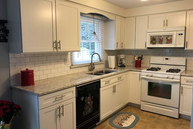 Large transitional l-shaped travertine floor and beige floor enclosed kitchen photo in New York with a double-bowl sink, shaker cabinets, white cabinets, quartzite countertops, white backsplash, subway tile backsplash, white appliances, no island and gray countertops