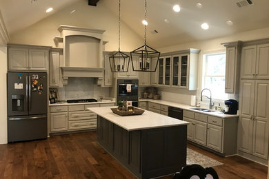 Example of a large transitional l-shaped dark wood floor and brown floor open concept kitchen design in Other with raised-panel cabinets, an island, a double-bowl sink, gray cabinets, white backsplash, subway tile backsplash, stainless steel appliances and white countertops
