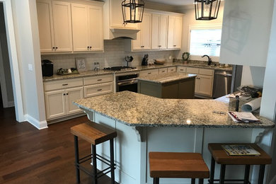 Inspiration for a large timeless u-shaped dark wood floor and brown floor enclosed kitchen remodel in Other with a double-bowl sink, shaker cabinets, white cabinets, granite countertops, white backsplash, subway tile backsplash, stainless steel appliances, a peninsula and multicolored countertops