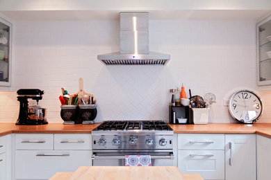 Example of a mid-sized trendy u-shaped eat-in kitchen design in Toronto with flat-panel cabinets, white cabinets, solid surface countertops, white backsplash, subway tile backsplash, stainless steel appliances and an island