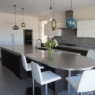 Design ideas for a large eclectic l-shaped open plan kitchen in Orange County with a double-bowl sink, flat-panel cabinets, white cabinets, glass benchtops, black splashback, glass tile splashback, stainless steel appliances, porcelain floors and with island.