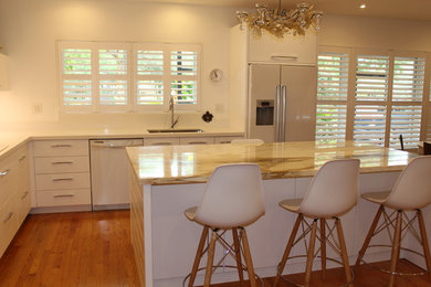 Mid-sized trendy u-shaped light wood floor open concept kitchen photo in Miami with an undermount sink, flat-panel cabinets, white cabinets, quartz countertops, white backsplash and white appliances