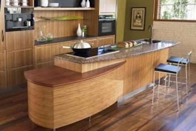 Foto de cocina comedor moderna de tamaño medio con puertas de armario de madera clara, encimera de granito, electrodomésticos negros, suelo de madera en tonos medios y una isla