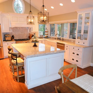 Design ideas for a large country l-shaped eat-in kitchen in Indianapolis with a farmhouse sink, raised-panel cabinets, beige cabinets, granite benchtops, grey splashback, stone tile splashback, stainless steel appliances, dark hardwood floors and with island.