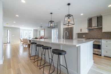 Example of a mid-sized transitional single-wall light wood floor and brown floor open concept kitchen design in Chicago with an undermount sink, shaker cabinets, white cabinets, marble countertops, brown backsplash, porcelain backsplash, stainless steel appliances, an island and white countertops