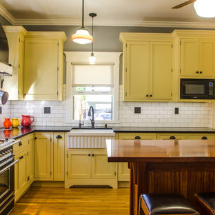 Ispirazione per una piccola cucina parallela minimalista chiusa con lavello stile country, ante con bugna sagomata, ante gialle, top in granito, paraspruzzi bianco, paraspruzzi con piastrelle diamantate, elettrodomestici da incasso, pavimento in legno massello medio e isola