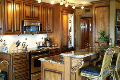 Imagen de cocina comedor lineal tradicional con armarios con rebordes decorativos, puertas de armario de madera oscura, encimera de granito, salpicadero beige, electrodomésticos de acero inoxidable y península