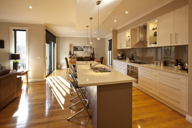 Exempel på ett avskilt, stort modernt u-kök, med en dubbel diskho, släta luckor, vita skåp, bänkskiva i kvarts, beige stänkskydd, glaspanel som stänkskydd, rostfria vitvaror, mellanmörkt trägolv och en köksö