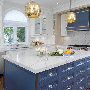 Inspiration for a transitional l-shaped kitchen in Toronto with quartz benchtops, a double-bowl sink, glass-front cabinets, white cabinets, white splashback, stainless steel appliances, medium hardwood floors and with island.