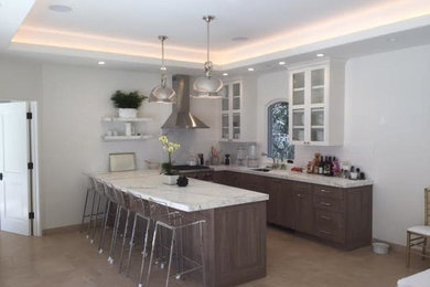 Mid-sized transitional u-shaped limestone floor open concept kitchen photo in San Francisco with a peninsula, an undermount sink, glass-front cabinets, white cabinets, quartzite countertops, white backsplash and stainless steel appliances