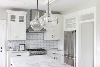 Example of a large transitional l-shaped enclosed kitchen design in Cedar Rapids with shaker cabinets, white cabinets, marble countertops, white backsplash, subway tile backsplash, stainless steel appliances and an island