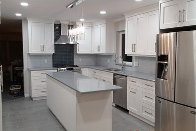 Bild på ett avskilt, mellanstort funkis l-kök, med en undermonterad diskho, skåp i shakerstil, vita skåp, bänkskiva i kvarts, grått stänkskydd, stänkskydd i glaskakel, rostfria vitvaror, vinylgolv, en köksö och grått golv