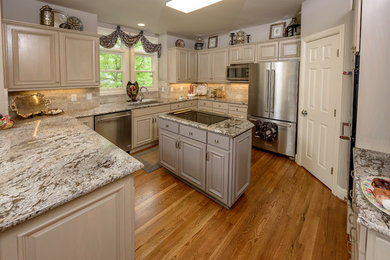 Mid-sized minimalist u-shaped medium tone wood floor and brown floor kitchen photo in Other with an undermount sink, raised-panel cabinets, gray cabinets, granite countertops, gray backsplash, porcelain backsplash, stainless steel appliances and an island