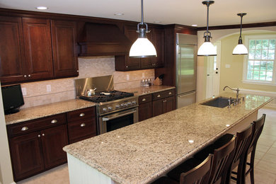 Single-wall travertine floor eat-in kitchen photo in New York with an integrated sink, raised-panel cabinets, dark wood cabinets, granite countertops, multicolored backsplash, ceramic backsplash, stainless steel appliances and an island