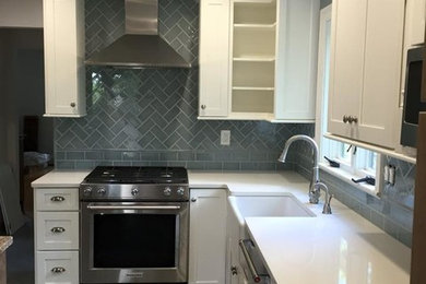 Mid-sized transitional u-shaped slate floor and gray floor enclosed kitchen photo in New York with an island, a farmhouse sink, shaker cabinets, white cabinets, quartz countertops, blue backsplash, subway tile backsplash and stainless steel appliances