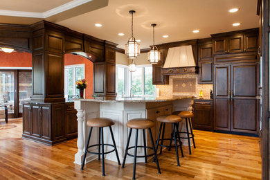 This is an example of a medium sized classic u-shaped enclosed kitchen in Minneapolis with a submerged sink, raised-panel cabinets, dark wood cabinets, granite worktops, white splashback, metro tiled splashback, stainless steel appliances, medium hardwood flooring, an island and brown floors.