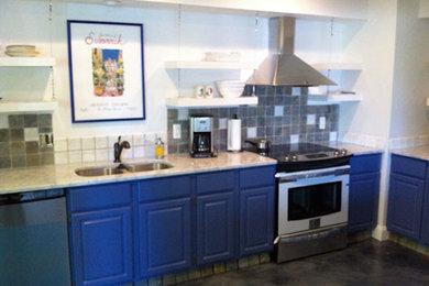 Modelo de cocina lineal grande con fregadero de doble seno, armarios con paneles con relieve, puertas de armario azules, salpicadero de azulejos de piedra y electrodomésticos de acero inoxidable