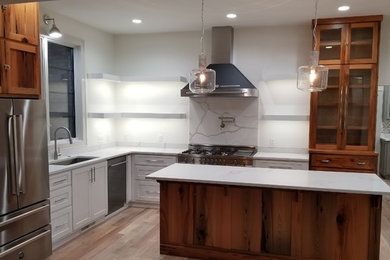 Photo of a medium sized traditional l-shaped kitchen in Other with a submerged sink, recessed-panel cabinets, white cabinets, marble worktops, white splashback, marble splashback, stainless steel appliances, light hardwood flooring, an island, brown floors and white worktops.