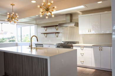 Inspiration for a large modern l-shaped kitchen in Los Angeles with a submerged sink, flat-panel cabinets, white cabinets, quartz worktops, beige splashback, porcelain splashback, stainless steel appliances, vinyl flooring, an island and brown floors.