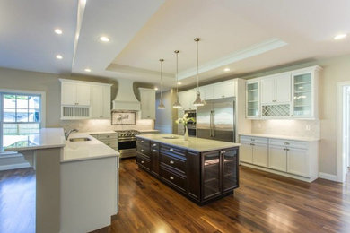 Large transitional l-shaped medium tone wood floor open concept kitchen photo in New York with an undermount sink, recessed-panel cabinets, white cabinets, solid surface countertops, white backsplash, stone tile backsplash, stainless steel appliances and an island