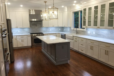 Mid-sized trendy u-shaped medium tone wood floor and brown floor kitchen photo in Boston with a farmhouse sink, shaker cabinets, white cabinets, quartz countertops, gray backsplash, stone tile backsplash, stainless steel appliances and an island
