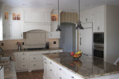 Mid-sized transitional l-shaped medium tone wood floor and brown floor open concept kitchen photo in Philadelphia with an undermount sink, raised-panel cabinets, white cabinets, granite countertops, beige backsplash, stone tile backsplash, white appliances and an island