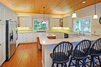 Inspiration for a mid-sized timeless u-shaped medium tone wood floor and brown floor eat-in kitchen remodel in Seattle with a double-bowl sink, recessed-panel cabinets, white cabinets, beige backsplash, ceramic backsplash, stainless steel appliances, an island and solid surface countertops