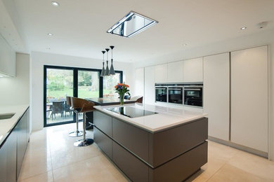 Inspiration for a large modern galley open plan kitchen in Kent with flat-panel cabinets, white cabinets, glass worktops, beige splashback, a breakfast bar, a built-in sink, glass tiled splashback, stainless steel appliances, slate flooring and beige floors.
