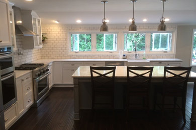Inspiration for a large craftsman l-shaped dark wood floor and black floor open concept kitchen remodel in Raleigh with a farmhouse sink, shaker cabinets, white cabinets, marble countertops, white backsplash, subway tile backsplash, stainless steel appliances and an island